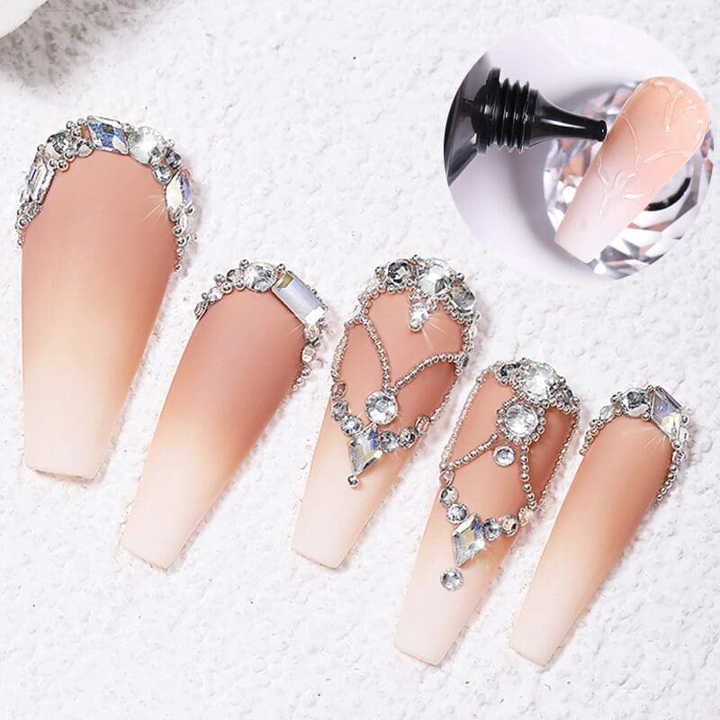 A set of five ornate, gradient nude acrylic nails adorned with intricate rhinestone designs and a close-up of black nail polish being applied using KYE 3-in-1 Nail Rhinestone Glue 30g.