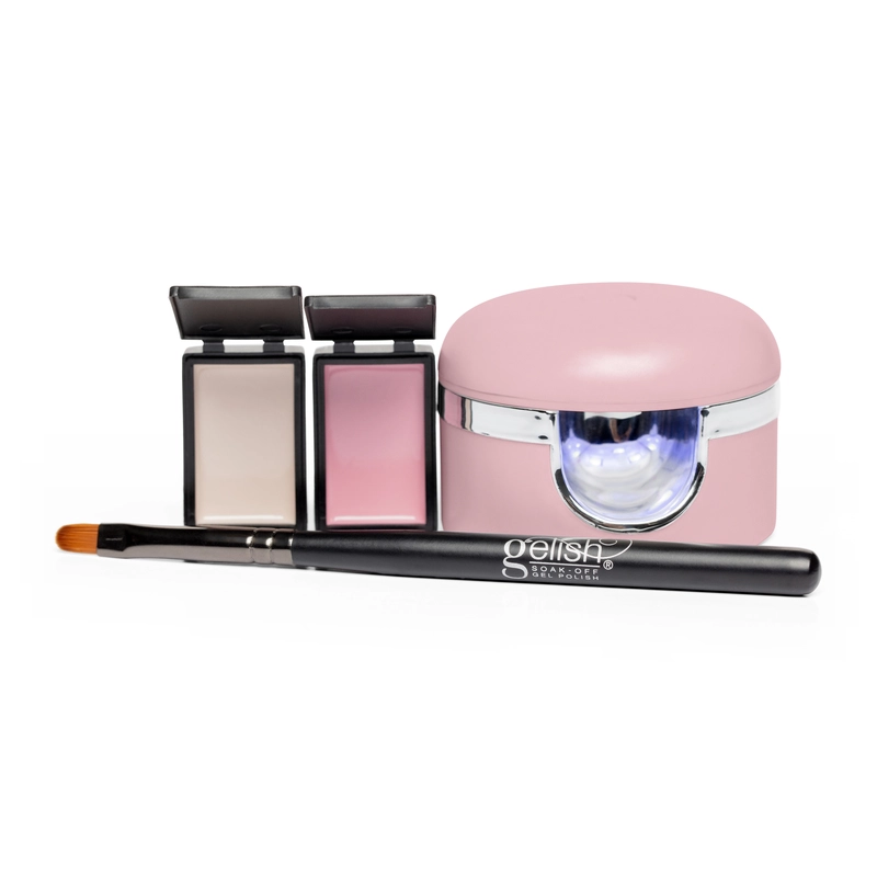 This image shows the Gelish Solid Cream Gel Polish Starter Kit - BLUSH, featuring a pink nail curing lamp, two small open compact cases with nail powders, and a black-handled nail brush labeled "Gelish," perfect for anyone starting their gel polish journey.